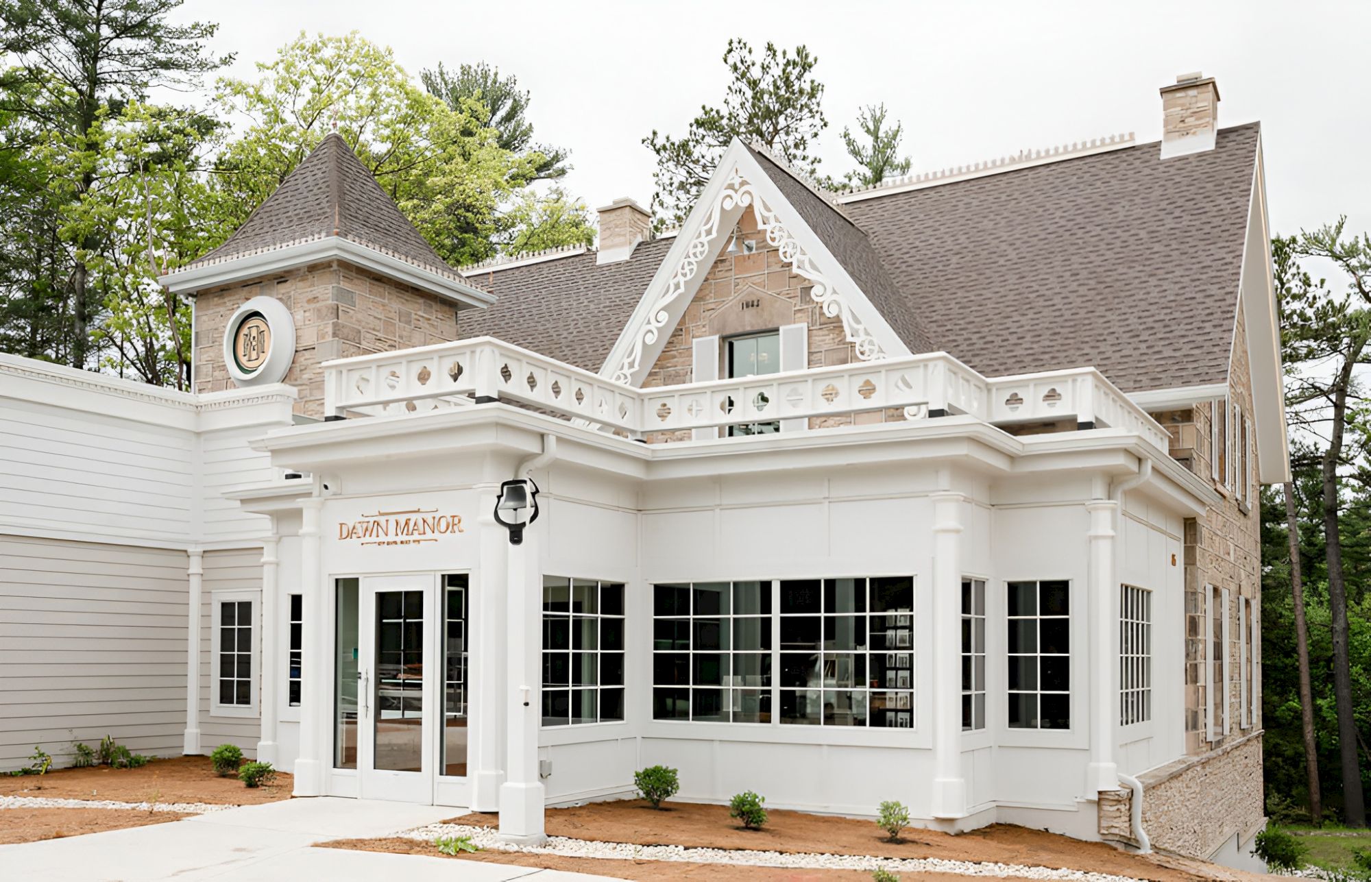 A white, charming clubhouse-style building with large windows, decorative trim, and a peaked roof, set among trees.