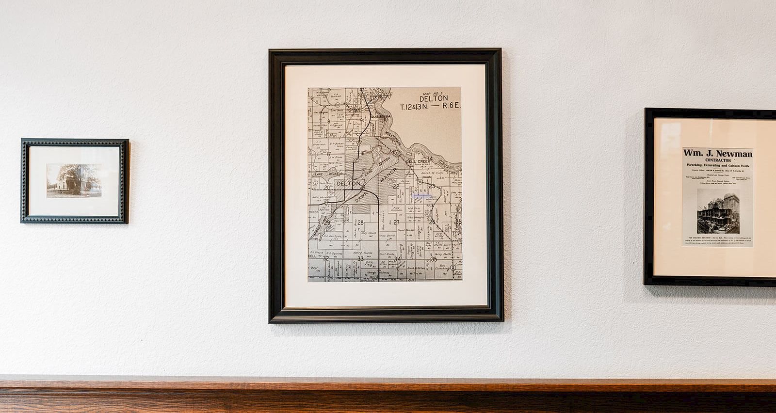 A wall with framed prints: a large map center, two smaller frames on the sides, all hung above a wooden ledge.