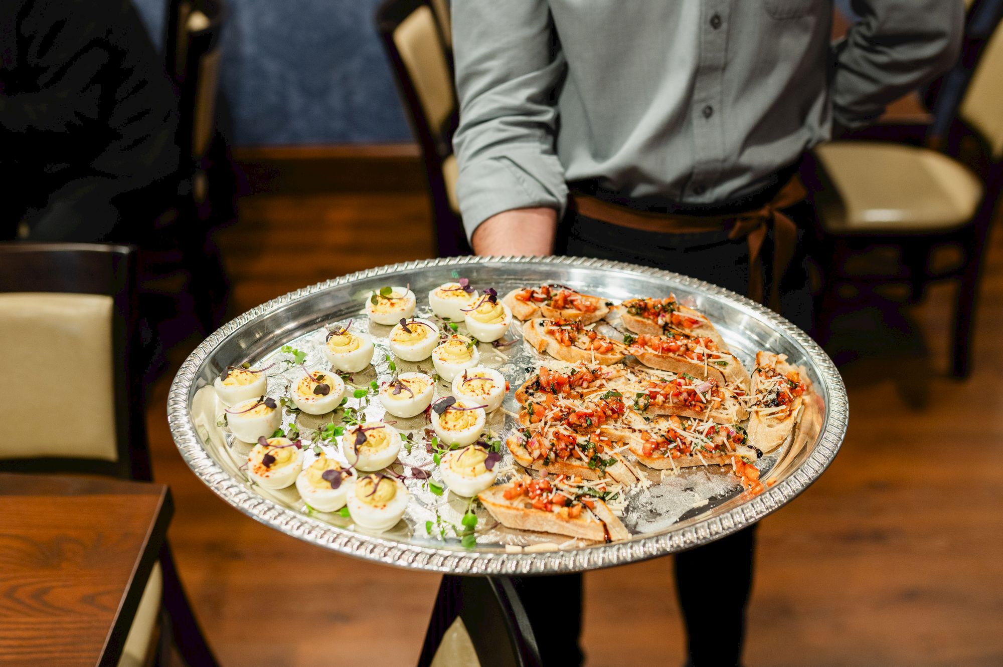 Dawn Manor server presents a platter of deviled eggs and bruschetta-style bites at a catered table, ready to serve.