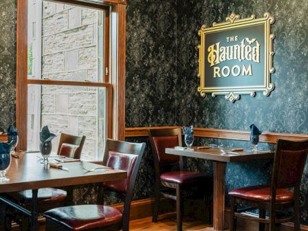 A cozy tavern with dark patterned walls, wooden tables and chairs, a framed map, and a sign that reads "Untitled Room."