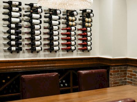Wine bottles on wall racks above a wooden bar with brick base; modern chandelier overhead.