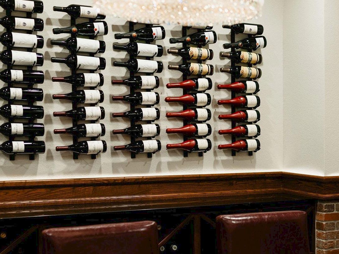 A wine rack displays rows of bottles on a wall, with brick lower wall, leather chairs, and a framed portrait above, in a cozy wine bar.