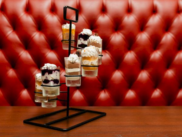 A metal stand holds several mini dessert cups&mdash;layered treats with whipped cream, fruit, and chocolate, arranged against a red tufted backdrop.