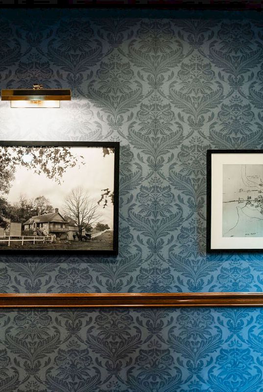 A blue-patterned gallery wall with two framed black-and-white photos and a wooden handrail running along the middle.