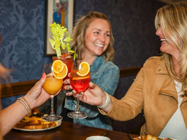 A group of friends toasting with colorful cocktails at a cozy restaurant, smiling and enjoying treats together.