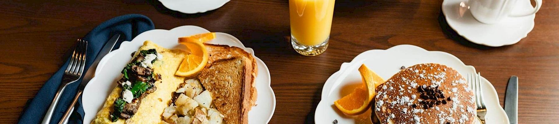 A breakfast spread with pancakes, toast, fruit, cereal, coffee, and orange juice on a wooden table, all set for three people, perfect for a morning meal.
