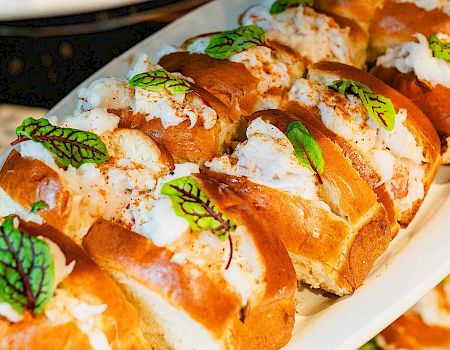 Delicious-looking sushi rolls or petit buns arranged on a white platter, topped with cream or cheese and fresh green herb leaves.