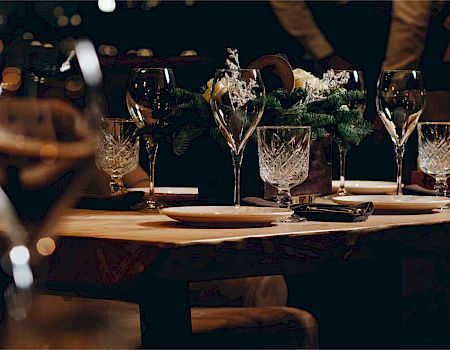 A dimly lit dining table set for a formal meal with champagne flutes, crystal glasses, plates, and greenery centerpiece, festive and elegant.