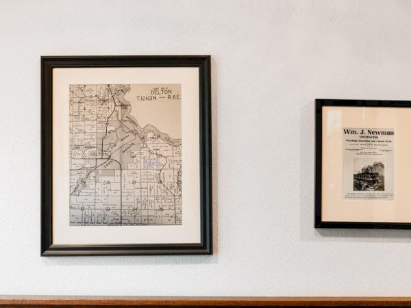 Two framed vintage maps hung on a white wall above a wooden mantle.