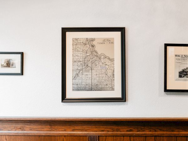 A wall with three framed prints/map art: a small frame left, a larger center map, and another print on the right, above a wooden shelf.