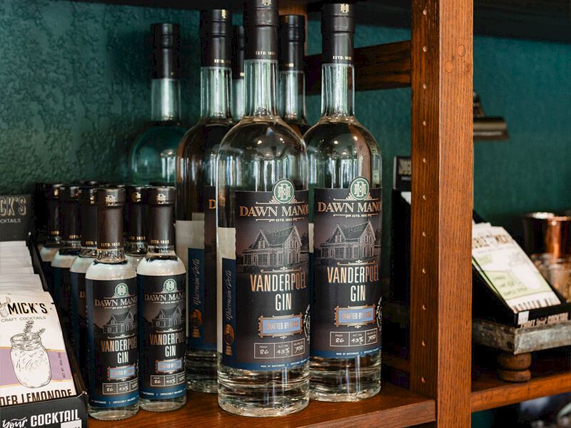 A display shelf of assorted bottles, including tall glass spirits with dark labels, arranged neatly among smaller boxes and items.