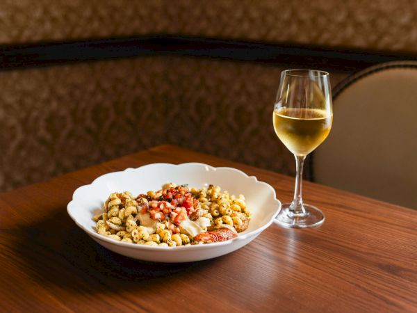 A bowl of mixed nuts and fruit salad on a wooden table, with a glass of white wine beside it, set in a cozy dining room.