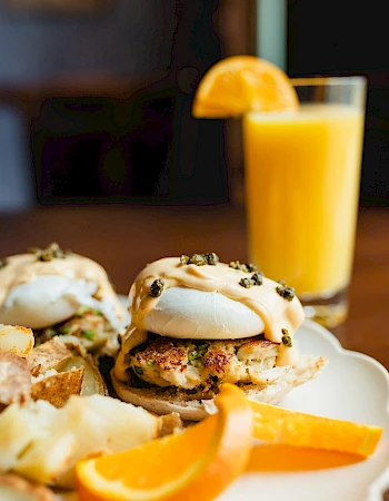 Seasoned mini burgers with soft buns, orange slices, and a tall glass of orange juice in the background.
