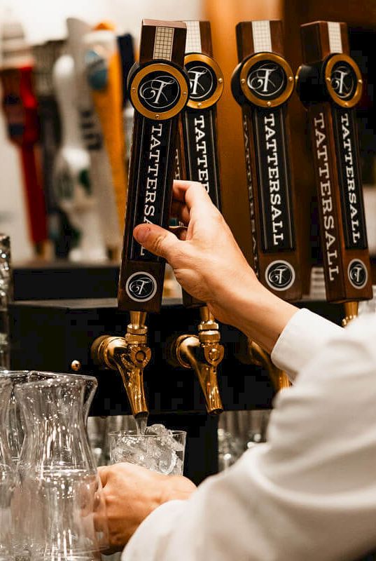 Someone pouring craft beer from taps at a bar, with glassware nearby, in a cozy pub setting.
