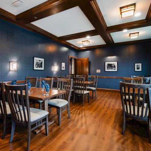 A stylish, compact kitchen and dining area with dark wood floors, blue walls, ceiling beams, a modern island, and a cozy, inviting dining table.