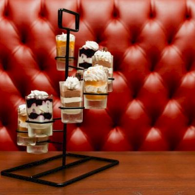 A metal display stand holds several mini pastries with whipped cream and berries, arranged on a red tufted backdrop.