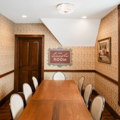 A modern, well-lit dining room with a wooden table and benches, decorative wall art, a large plant, and warm accents.