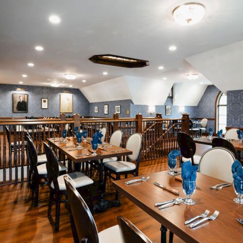 A bright dining area with a long wooden table, chairs around it, a chalkboard wall, shelves, and cozy ceiling lights in a homey kitchen/dining space.