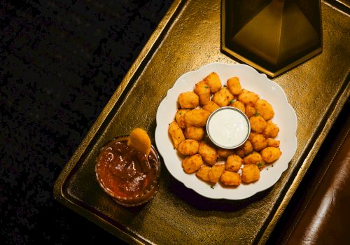 Plate of golden fried cheese bites with a dip in the center, plus a chocolatey sauce on the side, all on a decorative tray.