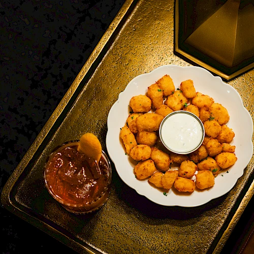 Plate of golden fried cheese bites with a dip in the center, plus a chocolatey sauce on the side, all on a decorative tray.