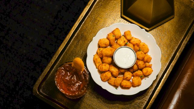 Plate of golden fried cheese bites with a dip in the center, plus a chocolatey sauce on the side, all on a decorative tray.