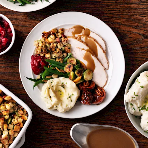 A platter of sliced meat with gravy, a fried egg, roasted Brussels sprouts, green beans, cranberries, and potato stuffing, ready to eat.