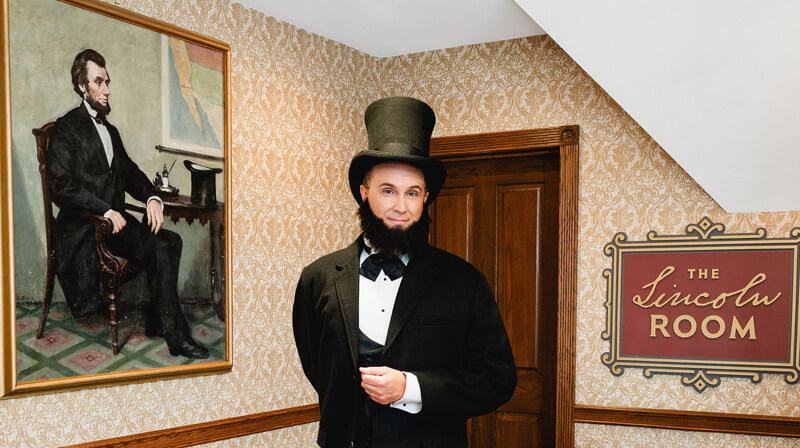 Man dressed up as Abraham Lincoln standing next to a portrait of Lincoln in the Lincoln Room