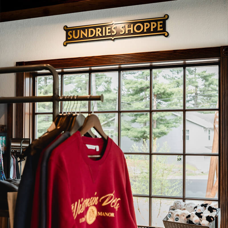 Sundries Shoppe sign and Dawn Manor branded crewnecks on clothing rack